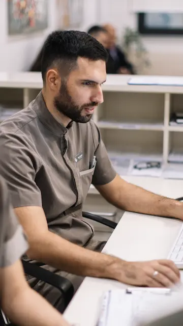 Administrative healthcare professionals work on the computer behind a front desk. Advance your career—learn more about our Health Services Online Program!