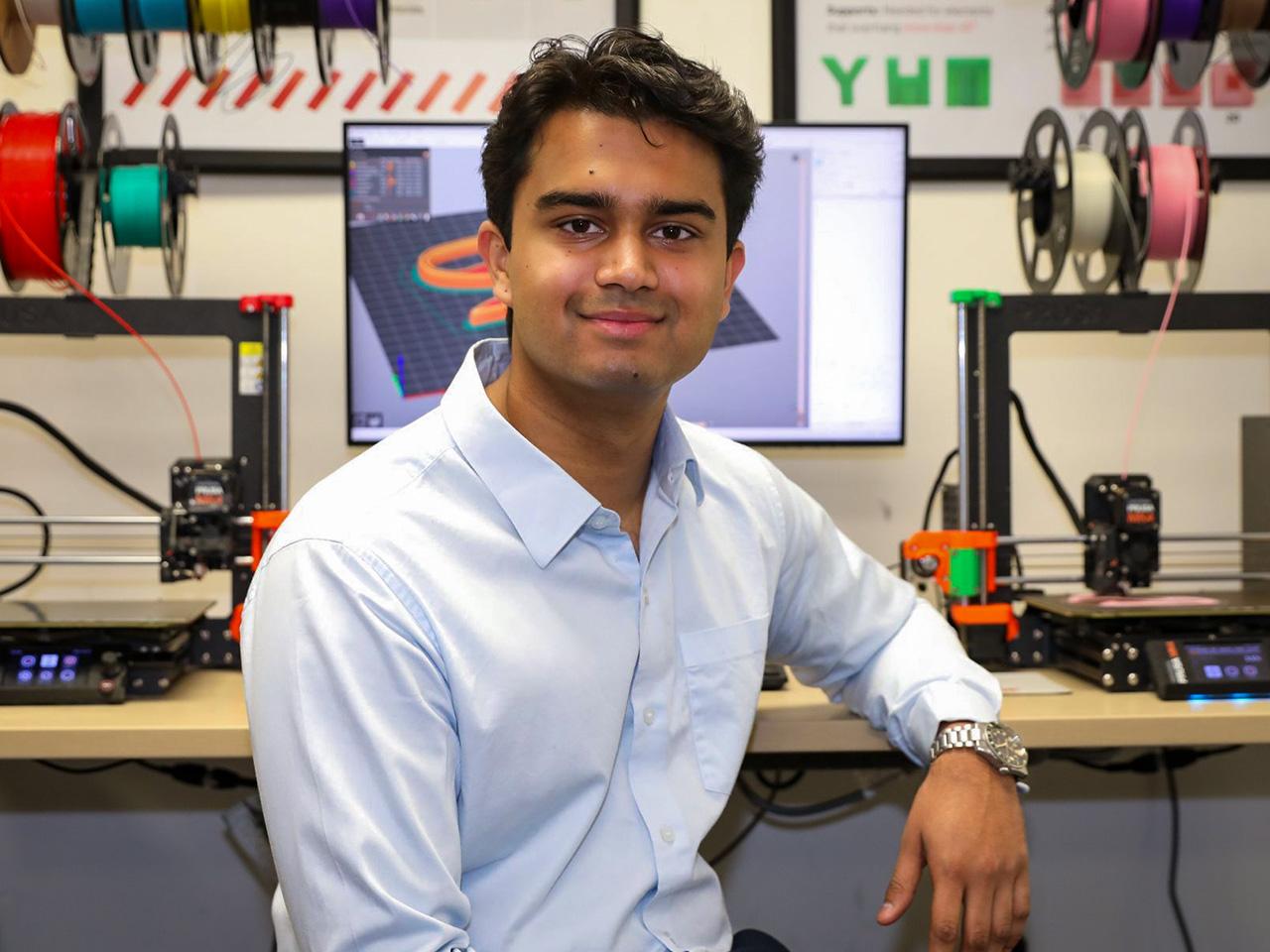 Nihal Patel sitting at a work desk with a computer display and 3d printers