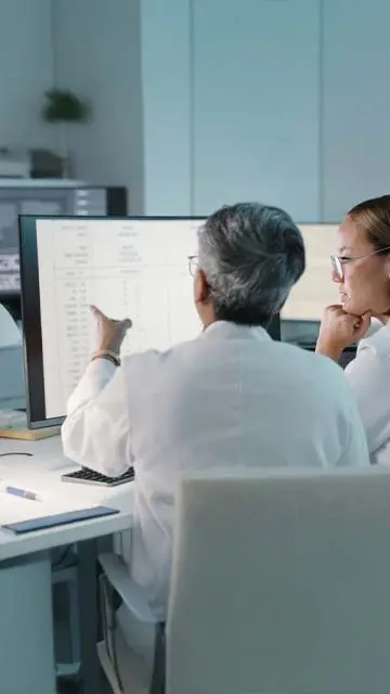 Two scientists in white coats examine data on a spreadsheet. 