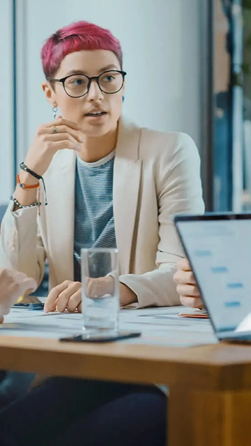 A diverse group of five people sitting around a small table conversing about a pie chart in a presentation on a laptop