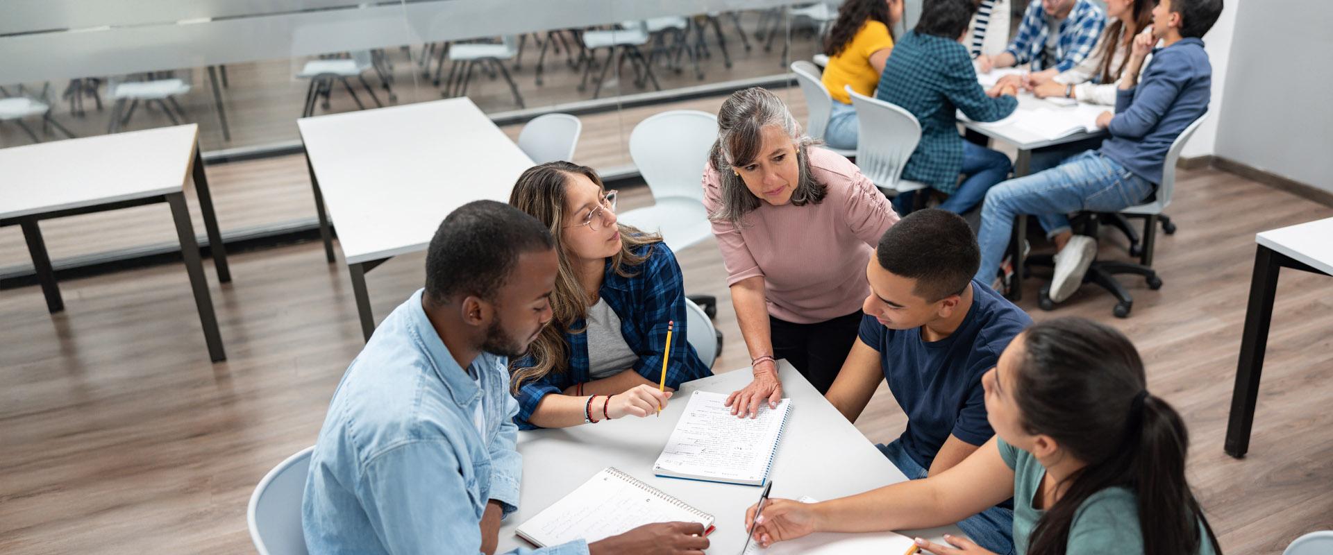 An instructor leans over a table to speak with a group of learners.