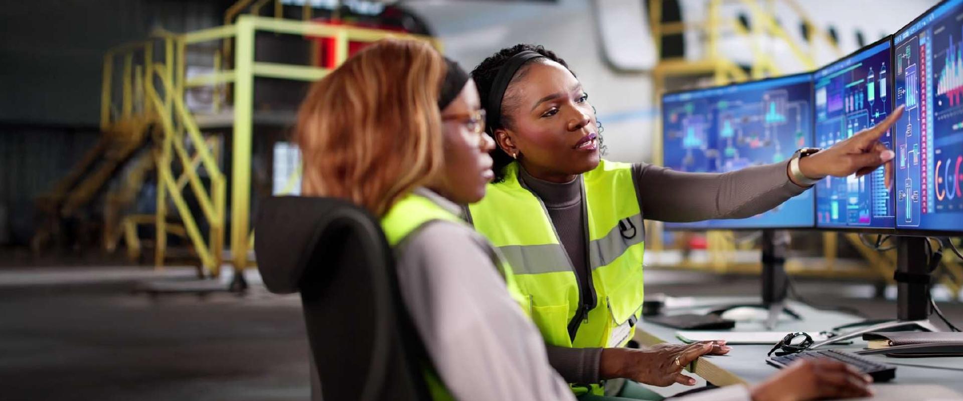 Two engineers sitting together, reviewing data on a large monitor. They are in an airplane hangar, and a plane is visible in the background.