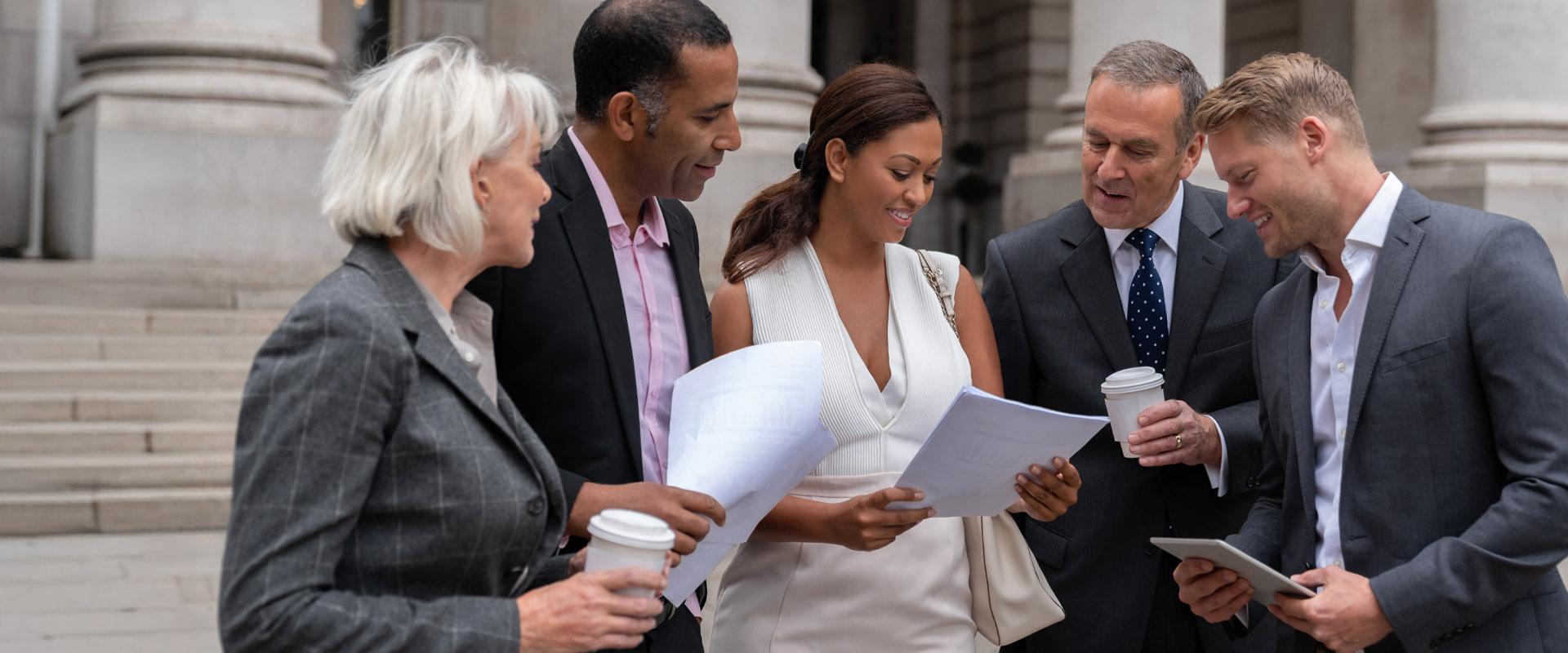 Smiling professionals wearing suits speaking outside courthouse. 