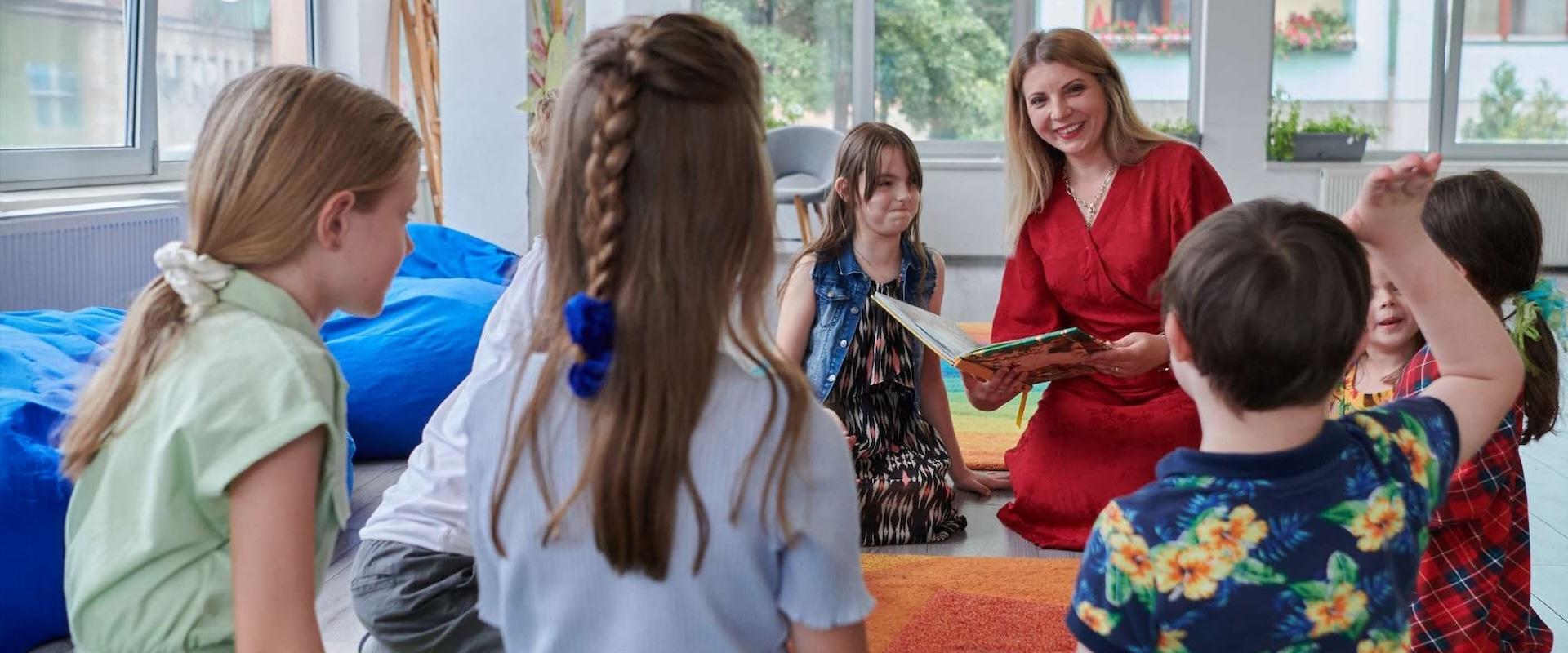 Smiling educator reads to elementary-aged students.