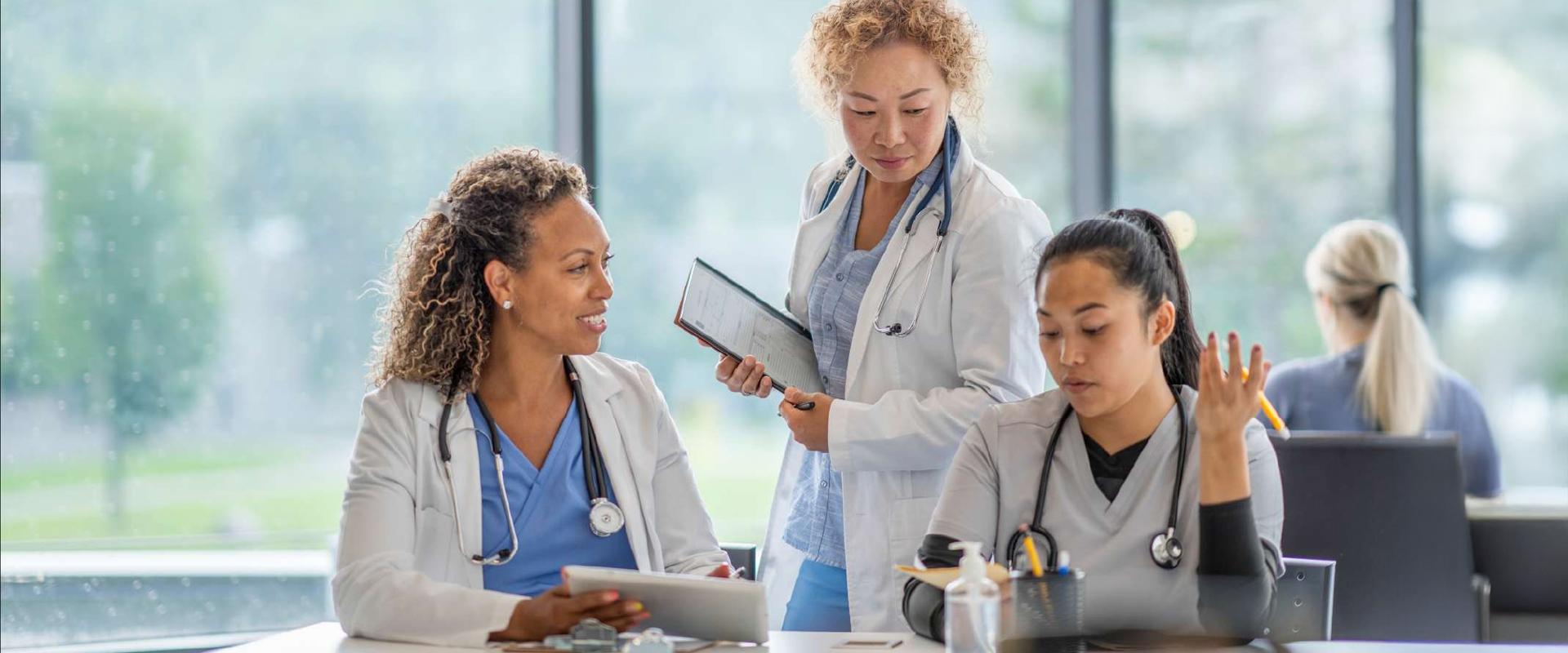A group of healthcare professionals in white coats having a conversation while reviewing a chart