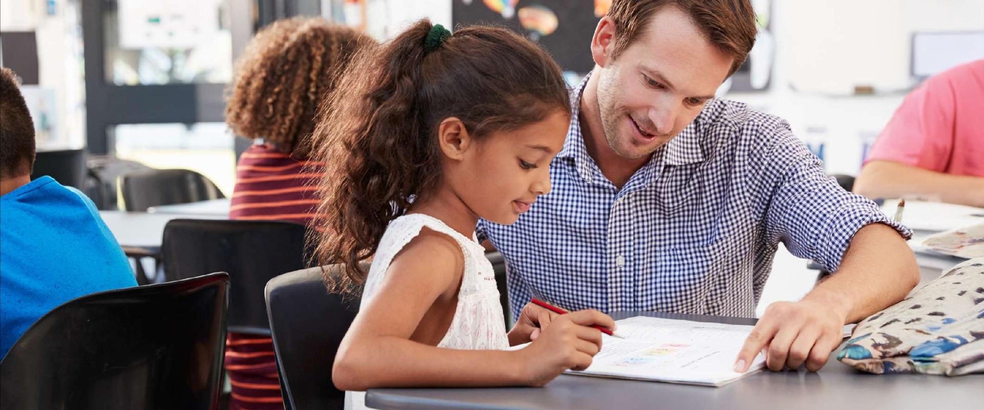 An adult education specialist works with a young person who is reading a book