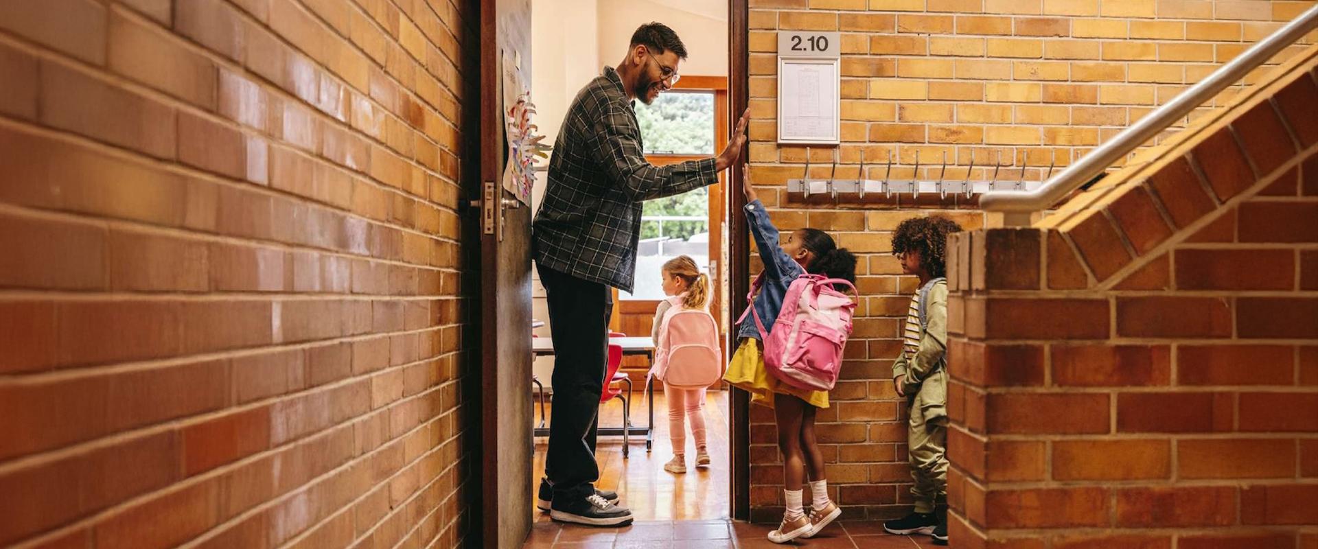 A teacher high-fiving young kids as the walk into their classroom