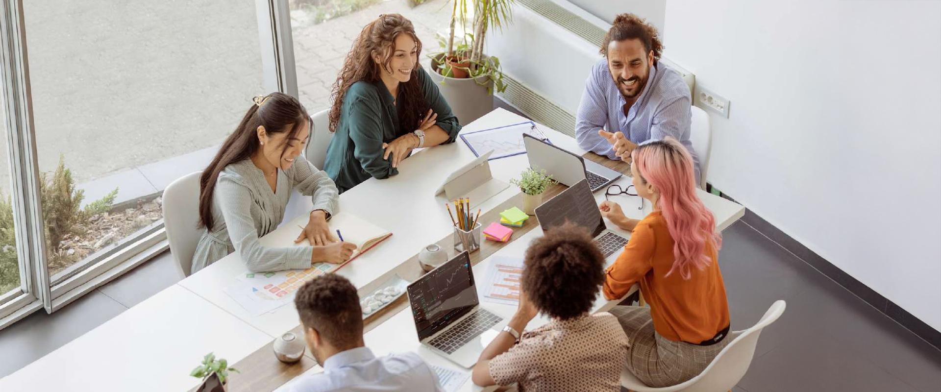 Diverse group of people in a team setting at a table reviewing laptops and materials 
