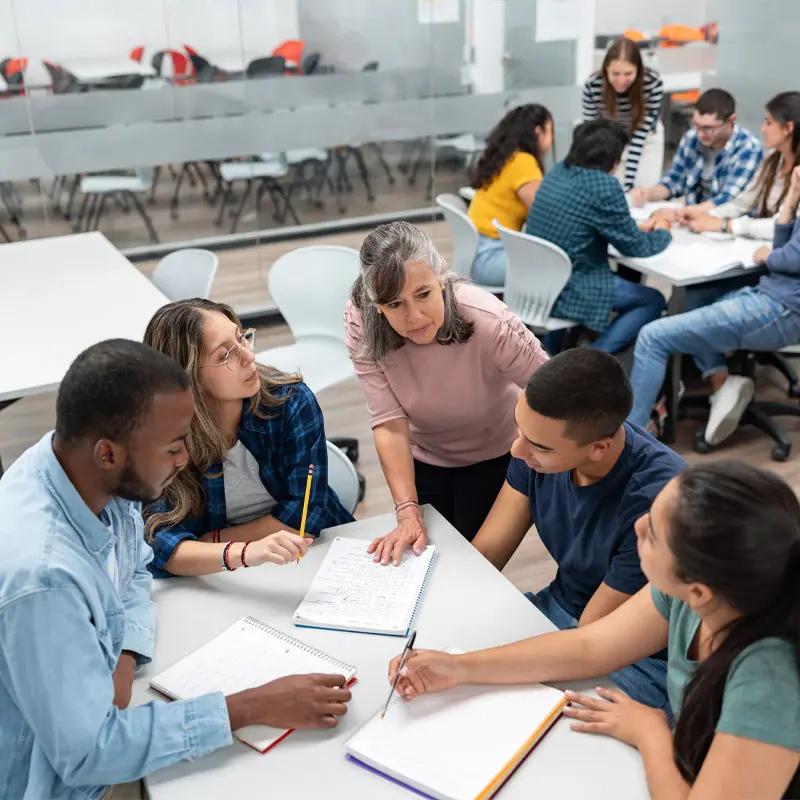 An instructor leans over a table to speak with a group of learners.