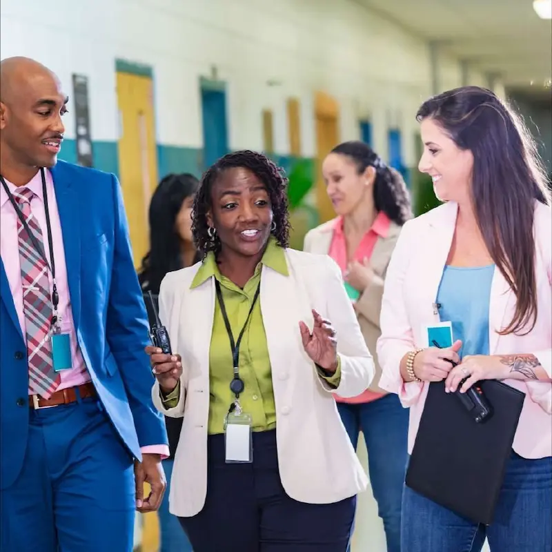 A group of three educators in semi-formal dress walk through the hallway of a school