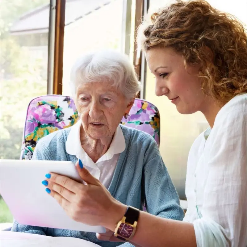 Professional, sitting beside their patient, reviewing the contents of a tablet together.