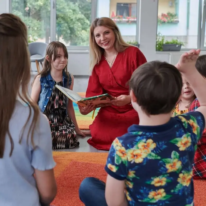 Smiling educator reads to elementary-aged students.