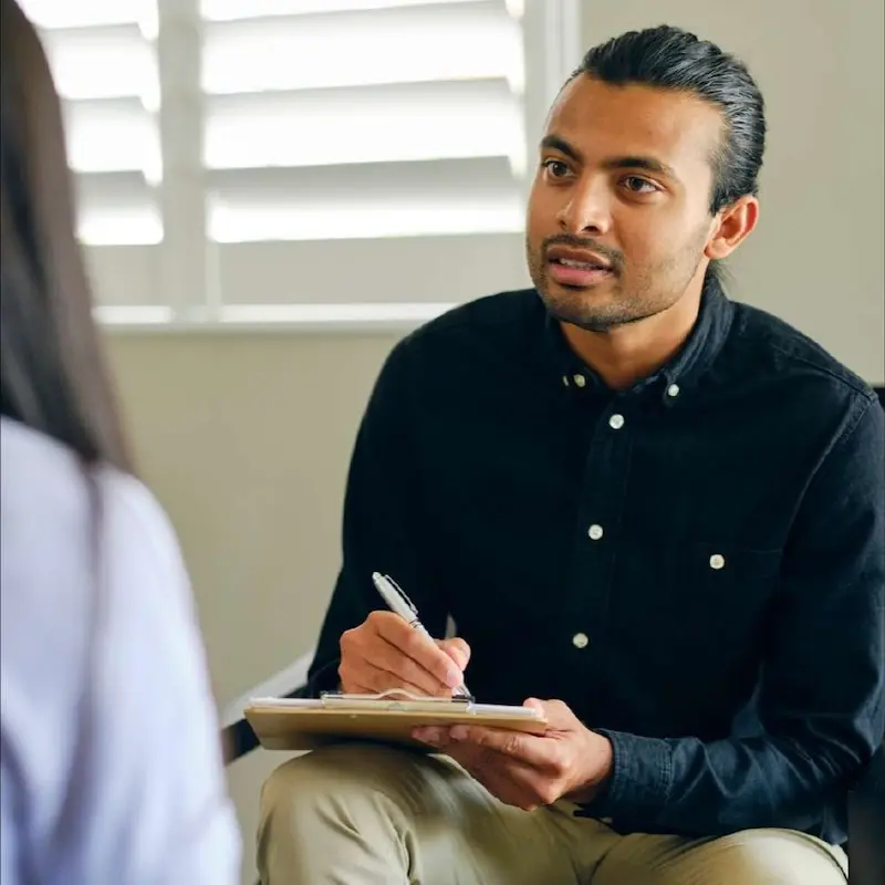 Specialist holding clipboard listening attentively to client during session.