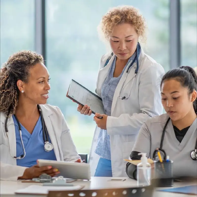 A group of healthcare professionals in white coats having a conversation while reviewing a chart