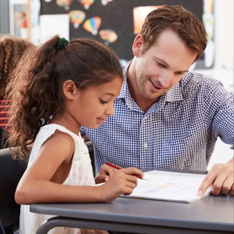 An adult education specialist works with a young person who is reading a book
