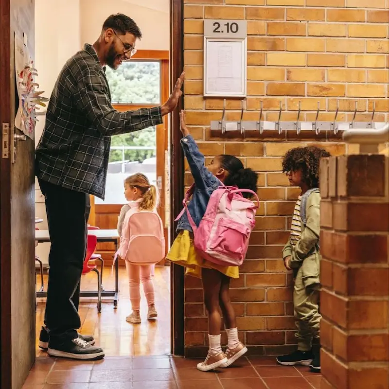 A teacher high-fiving young kids as the walk into their classroom