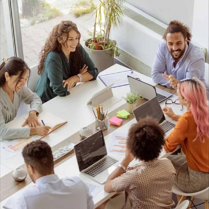 Diverse group of people in a team setting at a table reviewing laptops and materials 
