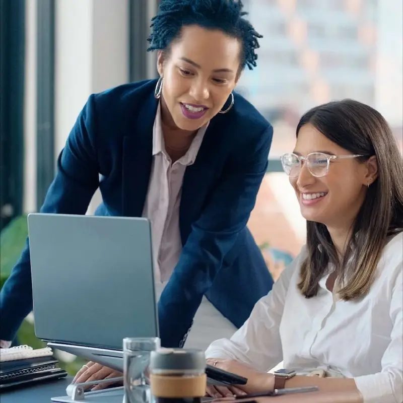 Two accountants work on a laptop and ipad. 