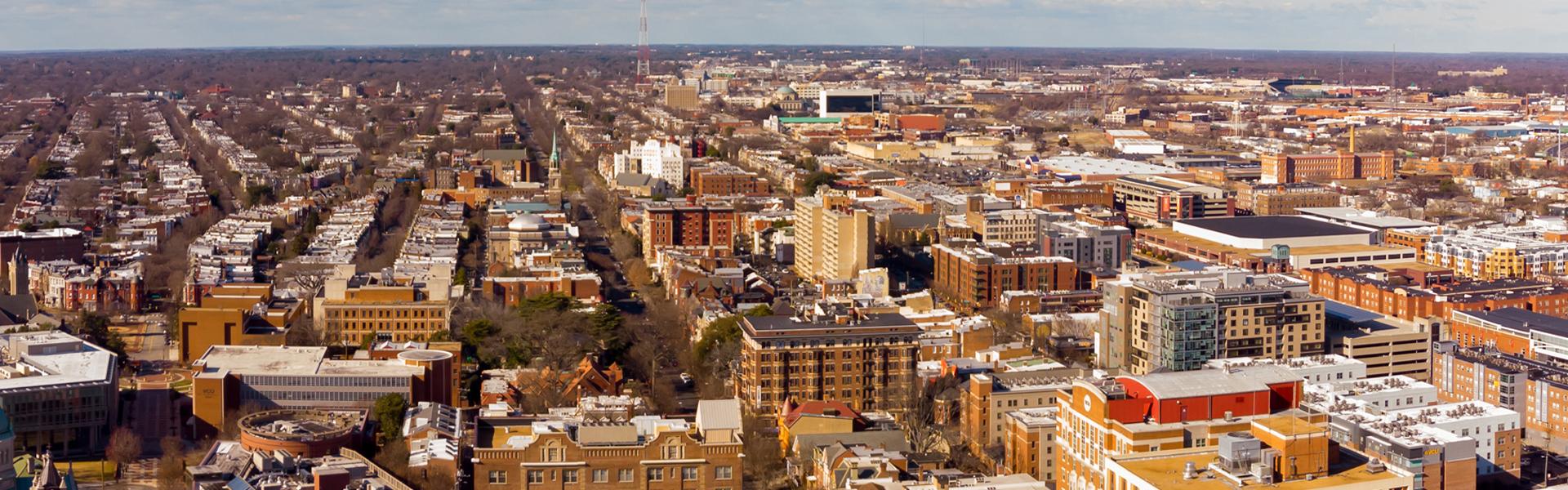 Overhead view looking west across VCU’s Monroe Park Campus and the surrounding Fan District, with rows of historic homes, mid-rise buildings and long tree-lined streets stretching toward the horizon.