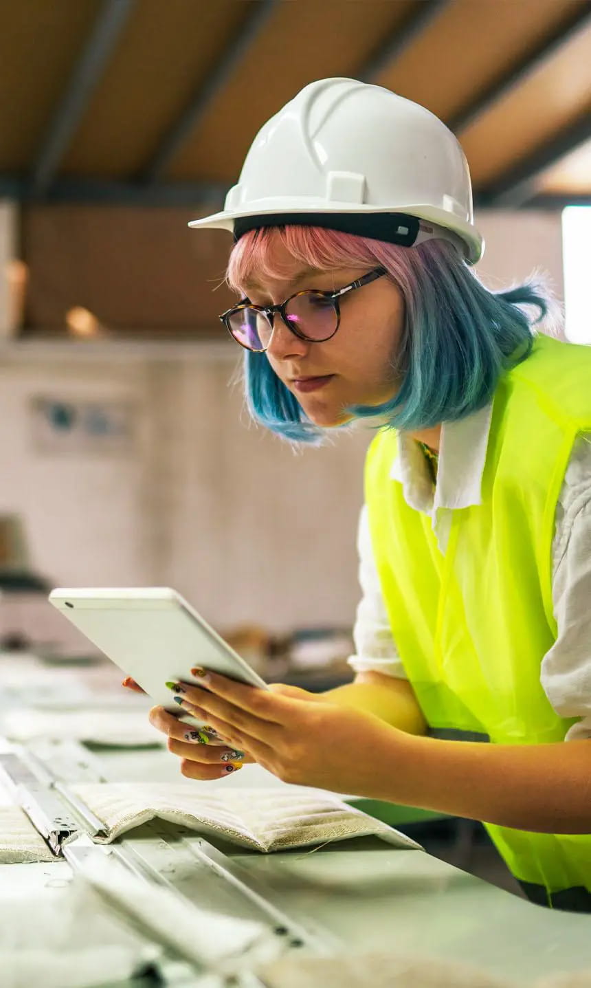 Person wearing a hard hat a yellow reflective vest looks at a mobile tablet